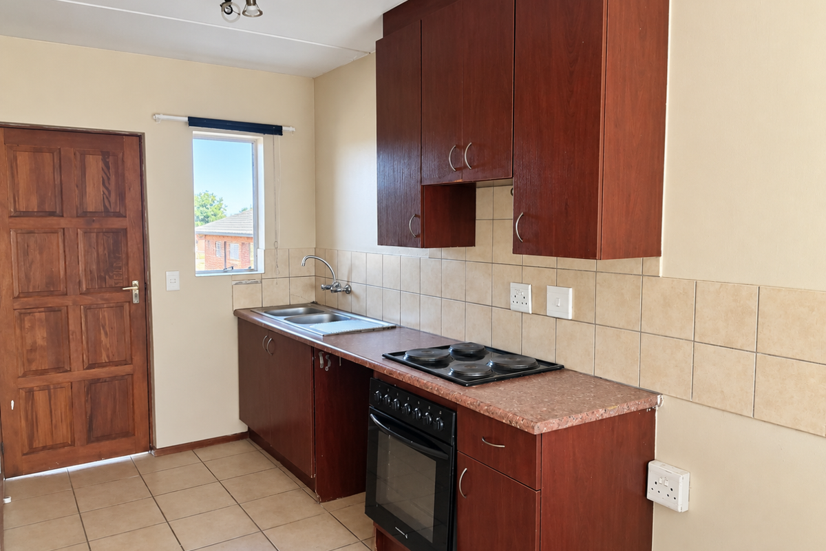 A functional kitchen featuring dark wood cabinetry, a built-in oven with electric hob, tiled backsplash, and neutral floor tiles.