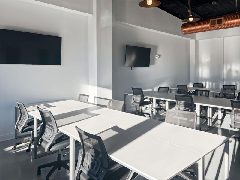 Modern open-plan office space featuring exposed industrial ductwork, pendant lighting, and wall-mounted screens, providing a clean and professional work environment.