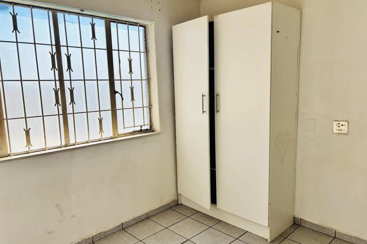 A bedroom featuring tiled flooring, a built-in wardrobe, and a window fitted with security bars, requiring cosmetic updates to the wall finishes.