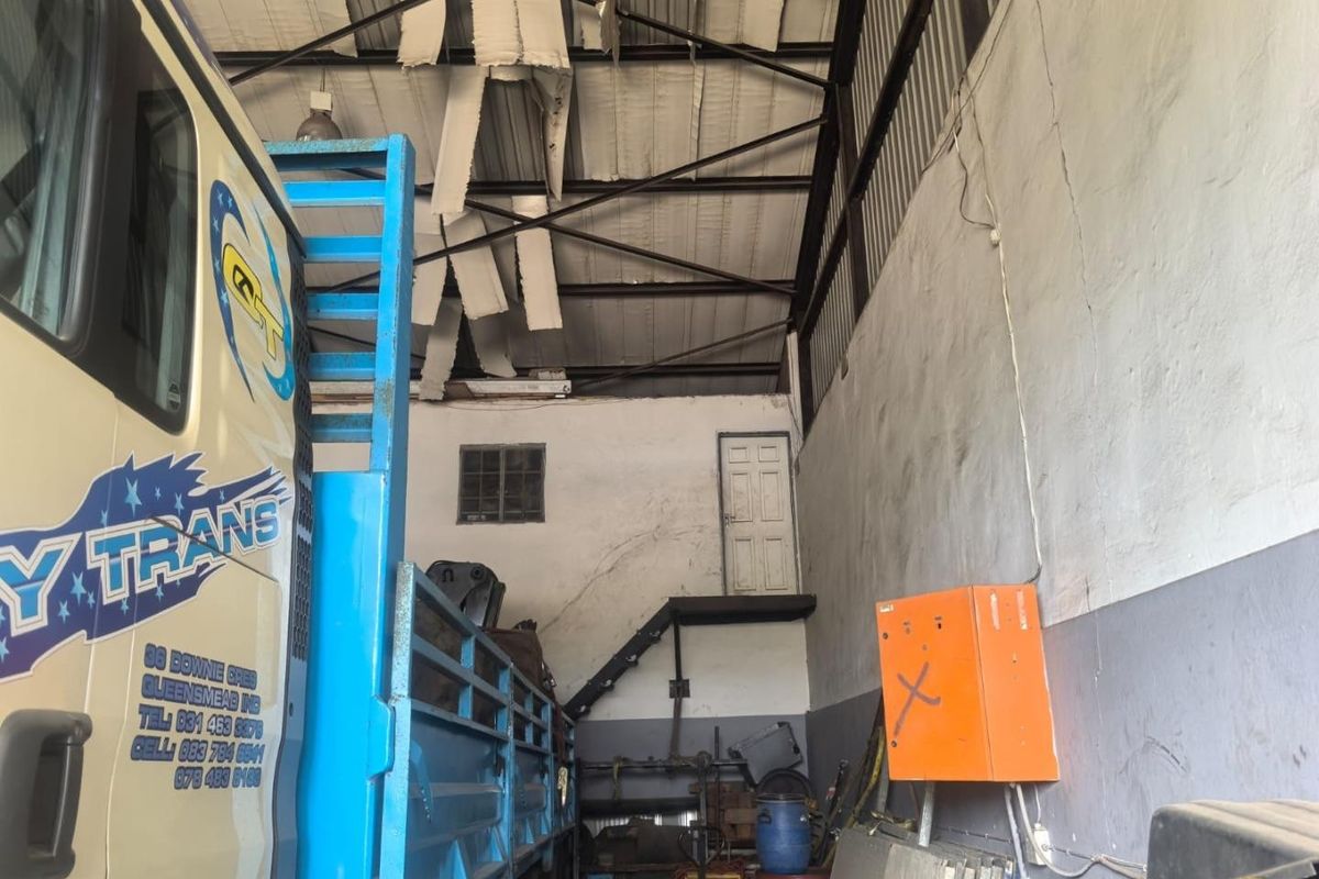 Industrial garage space featuring high ceilings with exposed steel trusses, a raised access door with steel stairs, and an electrical distribution board.