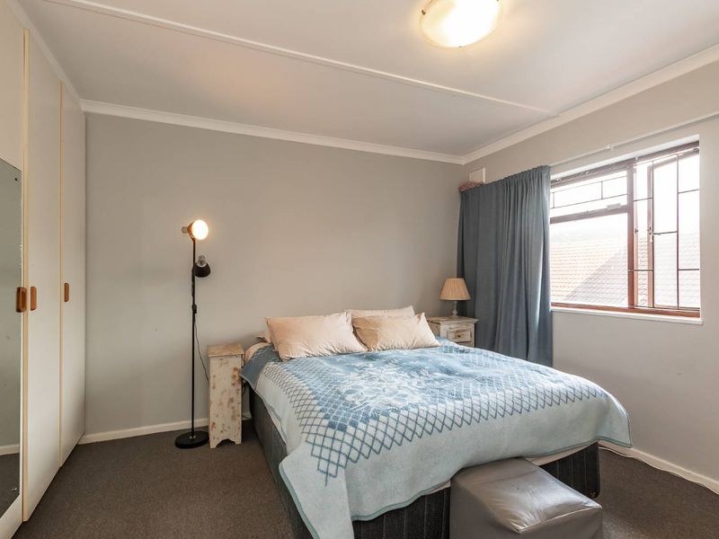 A functional bedroom featuring built-in wardrobes, carpeted flooring, and a window fitted with security bars.