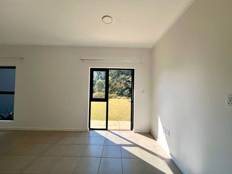 A bright, empty living room featuring neutral tiled flooring and a large aluminium sliding door providing direct access to the rear garden.