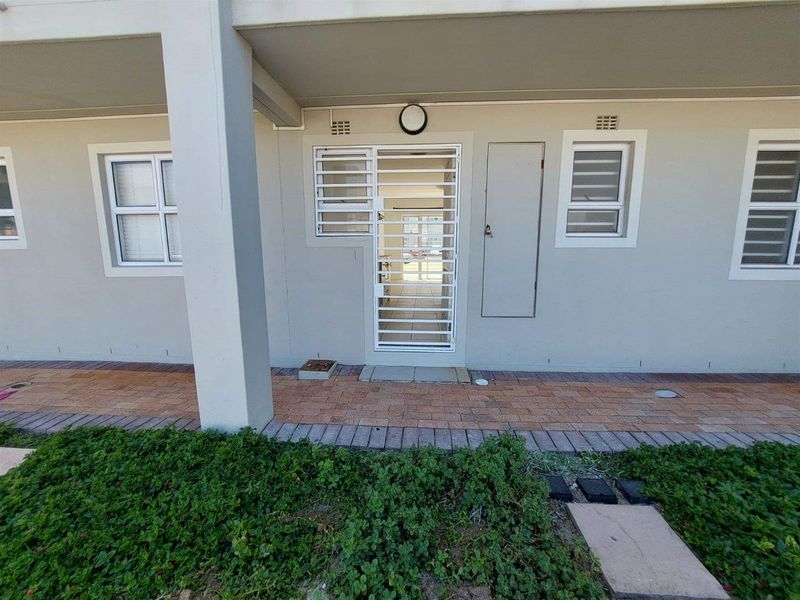 Exterior view of an apartment entrance featuring a security gate, paved walkway, and neutral facade finishes.