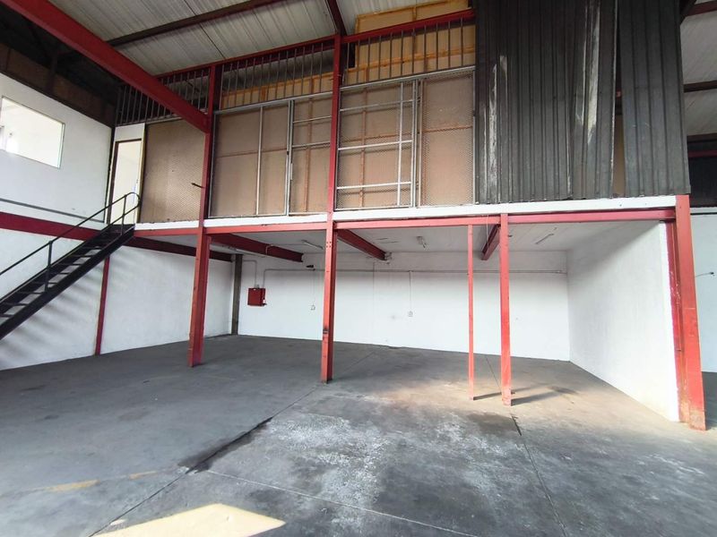 Industrial warehouse space featuring a steel mezzanine level, metal staircase, and open-plan concrete floor area suitable for storage or workshop use.