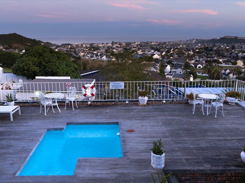 Elevated outdoor pool area featuring timber decking, safety railings, and panoramic views over the surrounding coastal neighborhood.