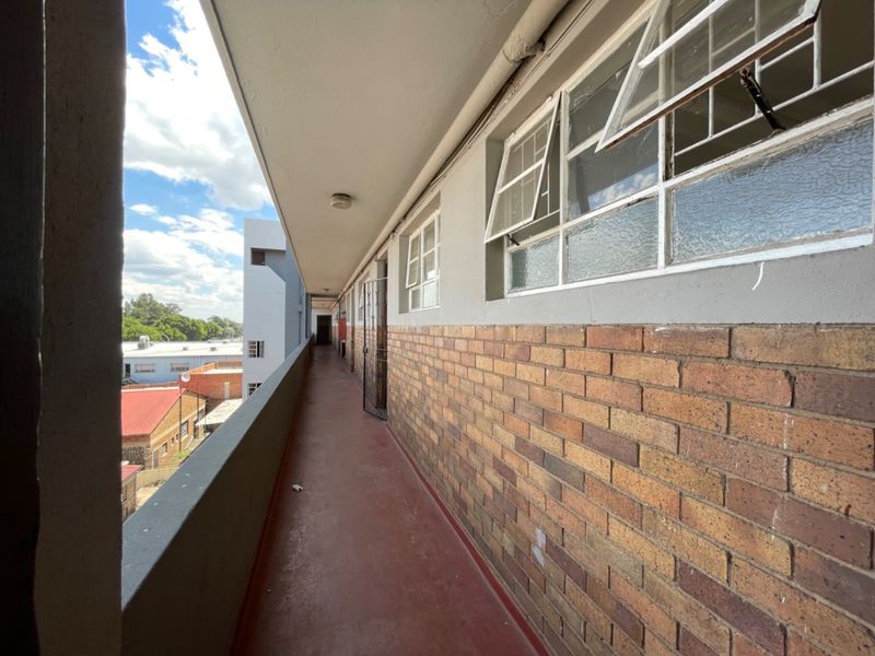 An exterior apartment walkway or balcony featuring brick wall finishes, steel-framed windows, and a concrete floor with views of the surrounding neighborhood.
