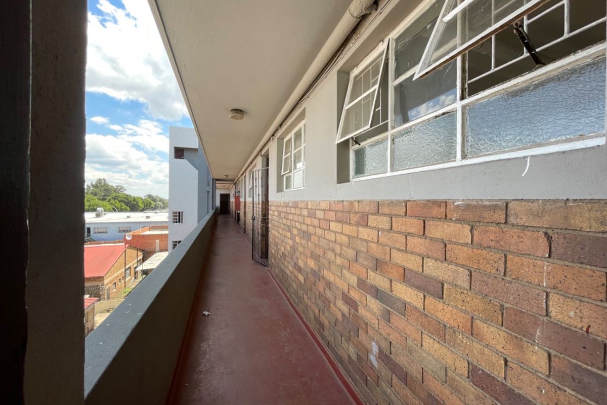 An exterior apartment walkway or balcony featuring brick wall finishes, steel-framed windows, and a concrete floor with views of the surrounding neighborhood.