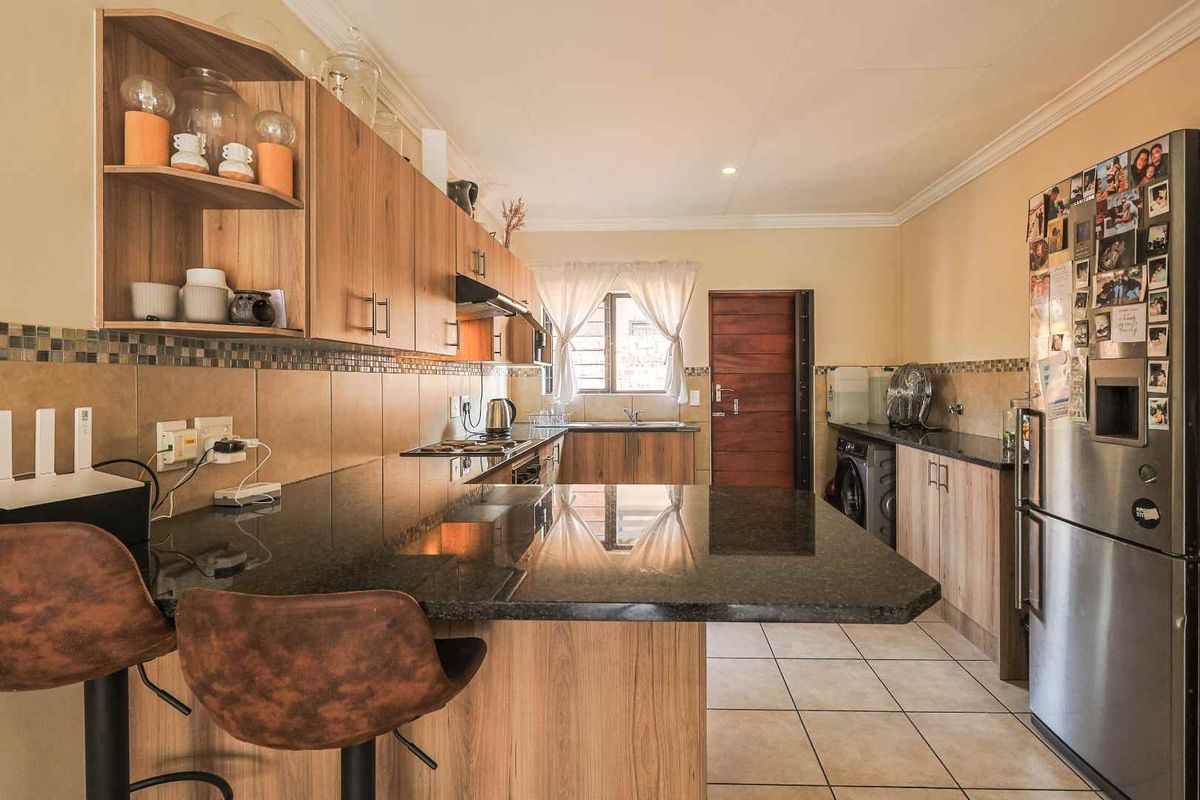 A functional kitchen featuring wood-look cabinetry, dark granite countertops, a tiled backsplash, and integrated space for laundry appliances.