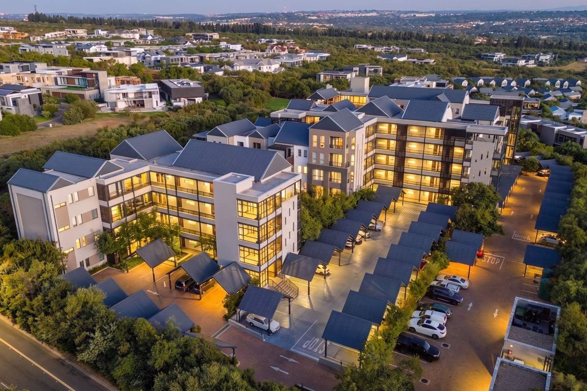 Aerial view of a modern multi-story apartment complex featuring extensive covered parking bays, paved driveways, and well-maintained exterior architecture at dusk.