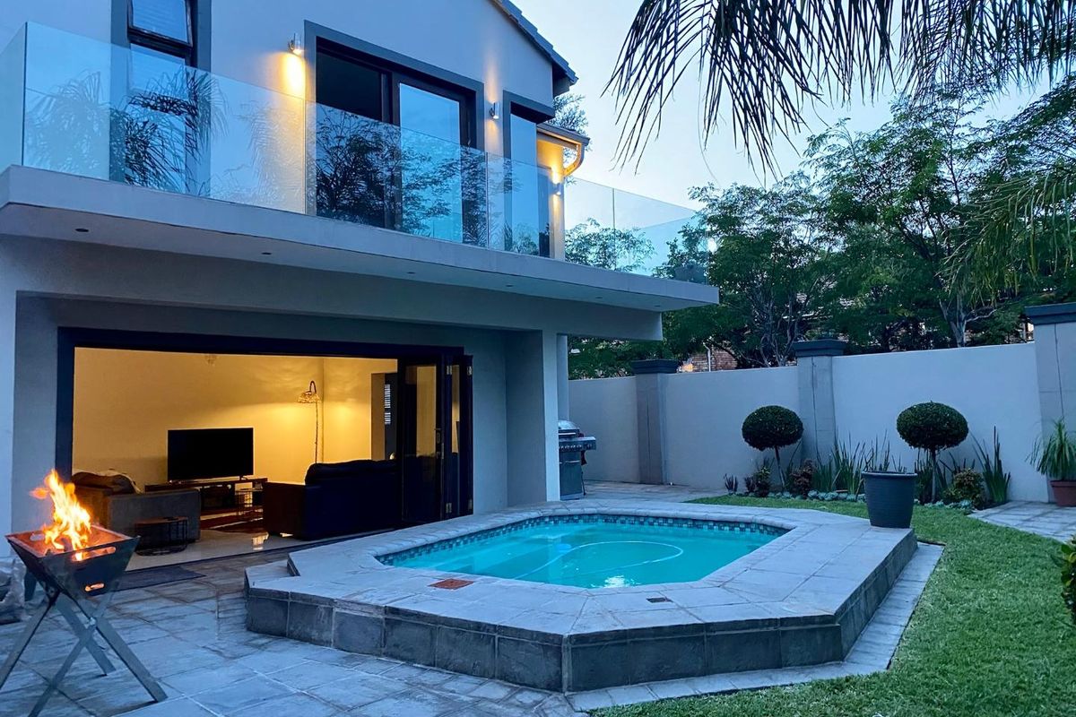 Rear exterior view featuring a paved patio, a built-in swimming pool, and a modern two-story home with glass balcony balustrades and sliding door access.