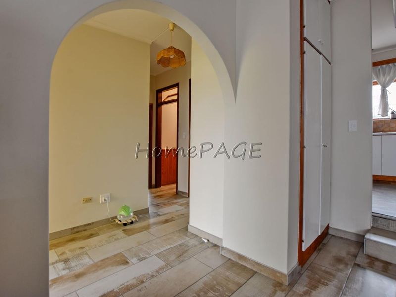 A bright hallway featuring an arched entryway, built-in storage cupboards, and neutral tiled flooring, leading towards other areas of the home.