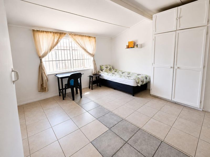 A functional bedroom featuring tiled flooring, a built-in wardrobe, and a window fitted with security bars.