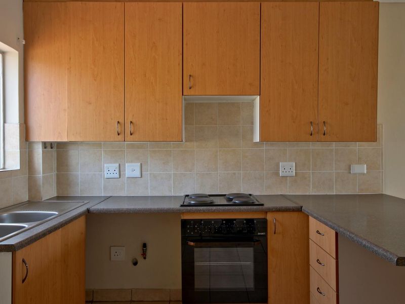 A functional kitchen featuring light wood-finish cabinetry, laminate countertops, a built-in oven with hob, and a stainless steel double sink.