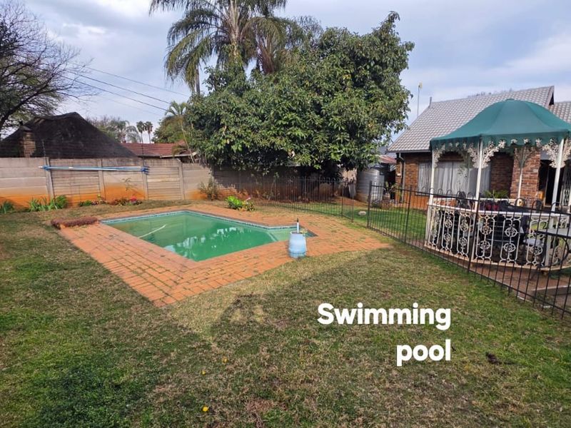Rear garden featuring a swimming pool with brick coping, enclosed by wrought iron fencing and a precast concrete boundary wall.