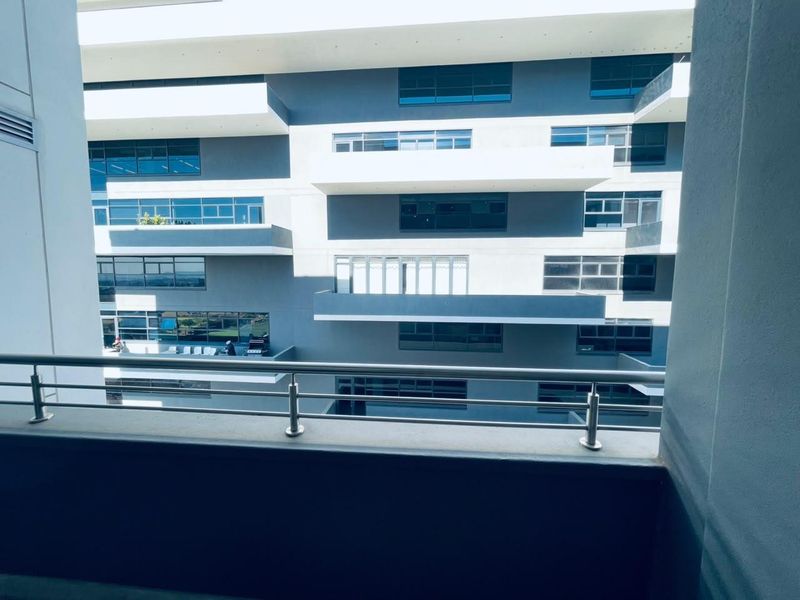 A view from a modern apartment balcony featuring a stainless steel balustrade, overlooking the building's exterior facade and adjacent units.
