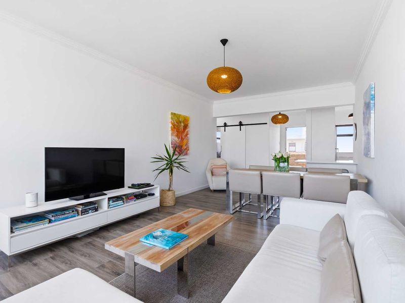 Bright open-plan living and dining area featuring modern laminate flooring, contemporary pendant lighting, and a stylish sliding barn door.