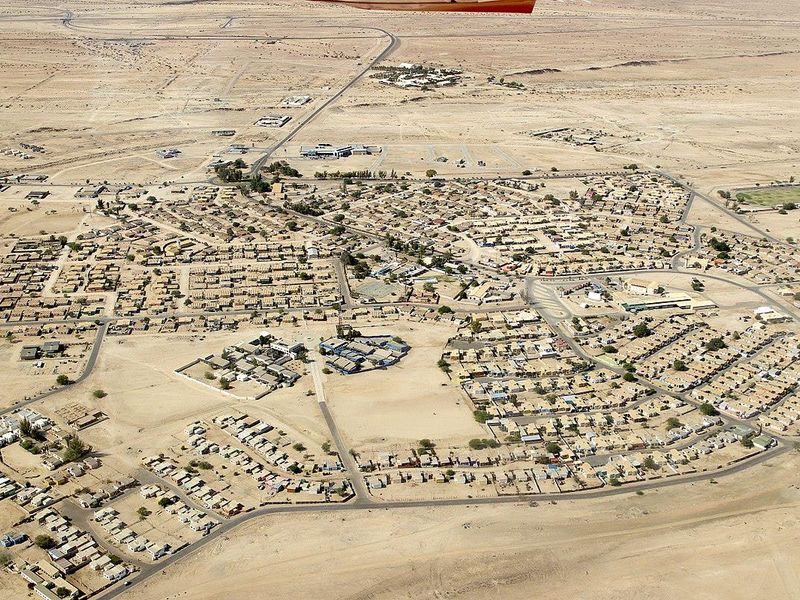 An aerial view of a desert residential and commercial development showing the layout of housing blocks and connecting road infrastructure.