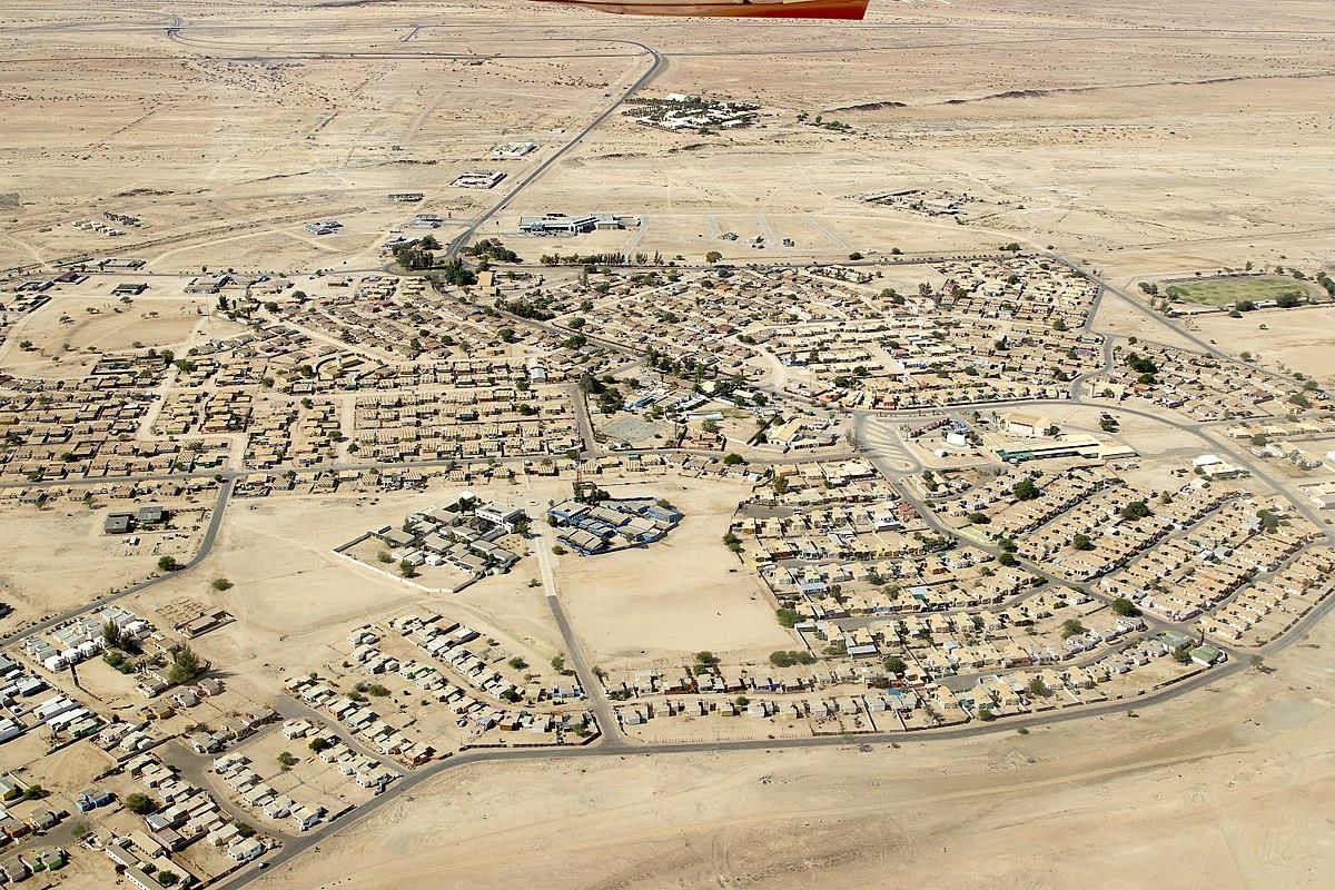 An aerial view of a desert residential and commercial development showing the layout of housing blocks and connecting road infrastructure.