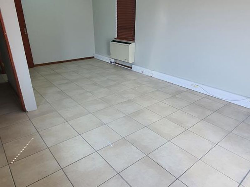 A vacant office space featuring neutral walls, tiled flooring, and a wall-mounted air conditioning unit, suitable for a professional workspace.