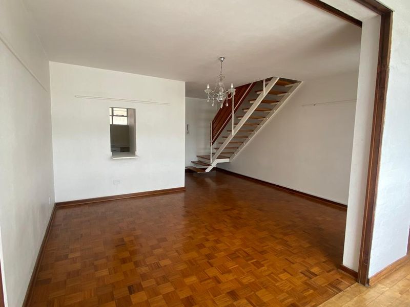 Spacious open-plan living area featuring classic parquet flooring, a central staircase, and a convenient serving hatch connecting to the kitchen area.