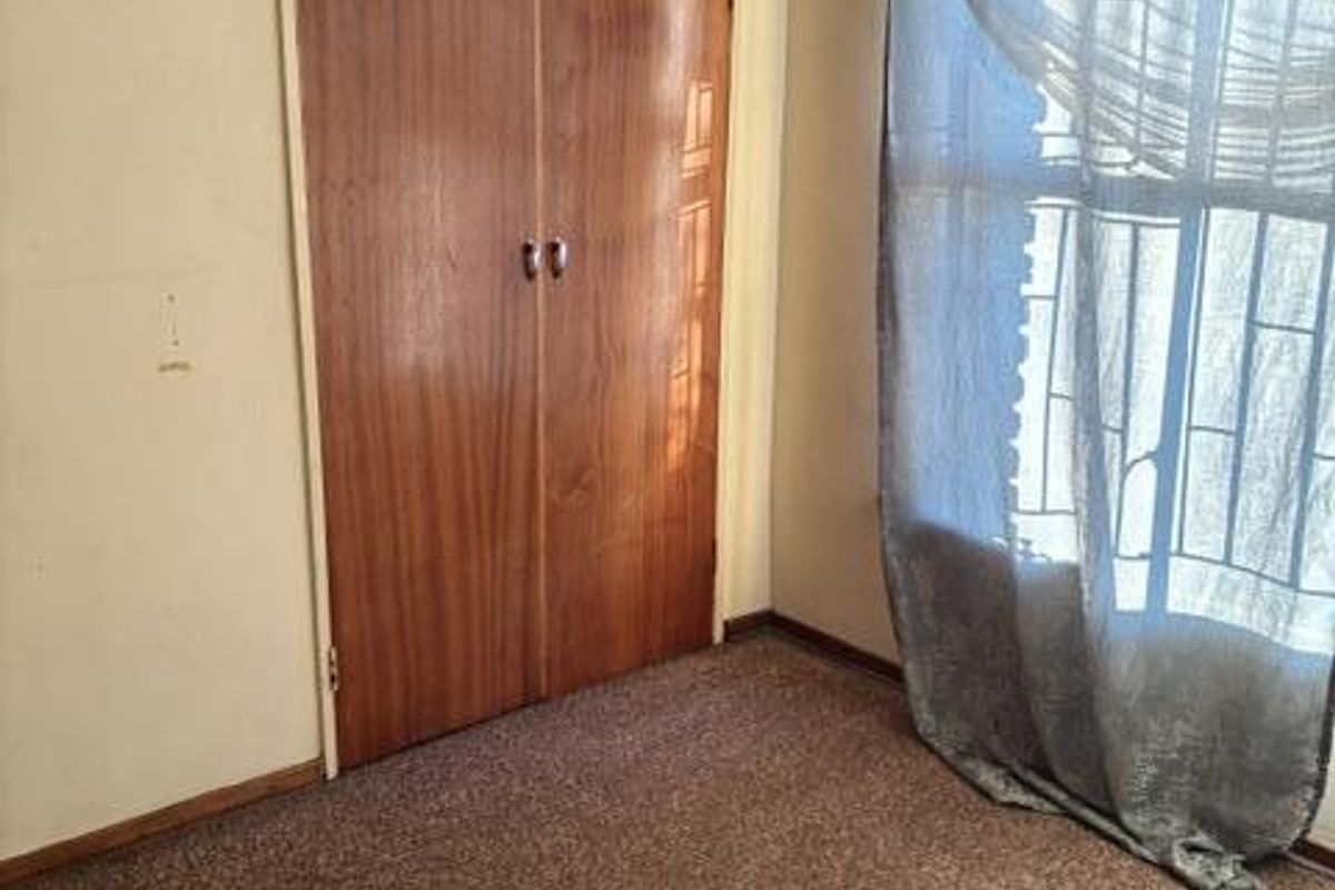 A bedroom featuring built-in wooden cupboards, carpeted flooring, and a window with security bars.