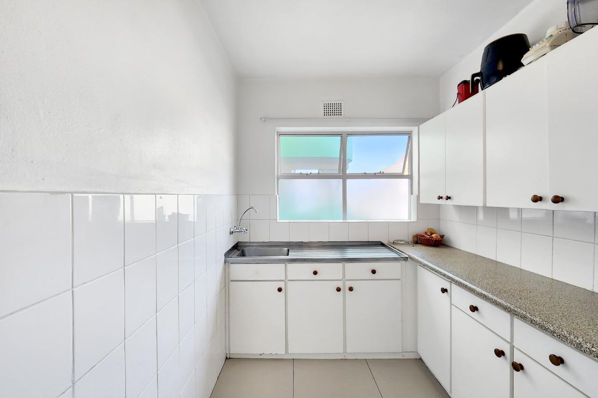 A functional kitchen featuring white cabinetry, a stainless steel sink, tiled splashbacks, and neutral floor tiles with a window for natural light.