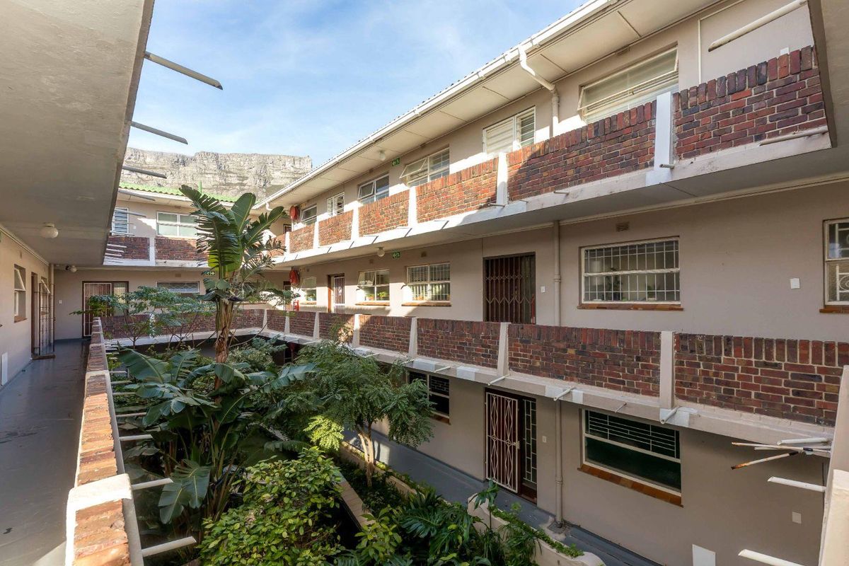 View of the apartment complex courtyard featuring brick balustrades, communal walkways, and established garden landscaping with mountain views in the background.