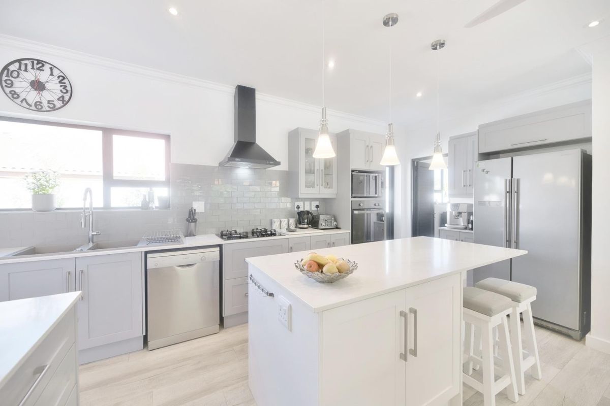 Modern kitchen featuring light grey shaker cabinetry, quartz countertops, a central island, subway tile backsplash, and integrated stainless steel appliances.