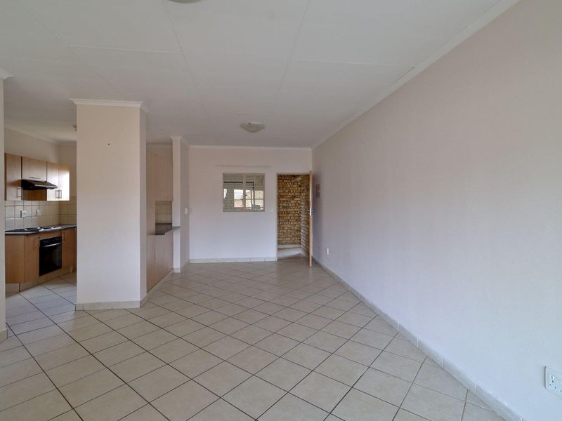An open-plan living and kitchen area featuring tiled flooring, built-in cabinetry, and a breakfast counter, presenting a clean, vacant space ready for personalization.