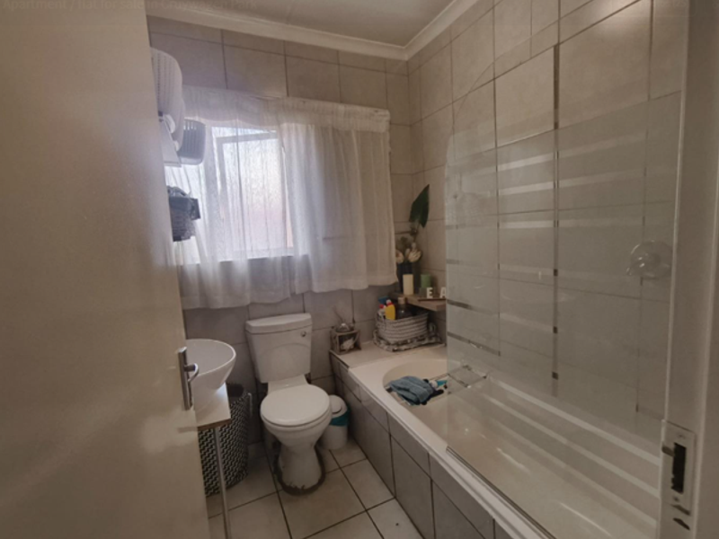 A functional bathroom featuring a bathtub with a glass screen, a pedestal basin, and a toilet, finished with neutral wall and floor tiling.