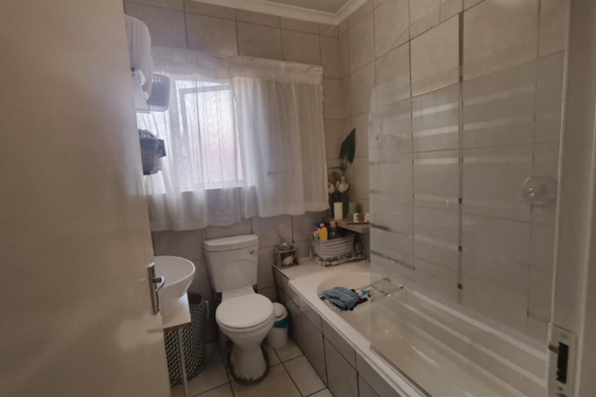 A functional bathroom featuring a bathtub with a glass screen, a pedestal basin, and a toilet, finished with neutral wall and floor tiling.