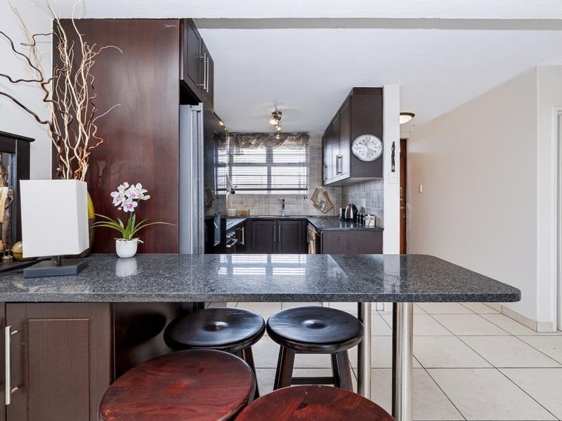 Open plan kitchen featuring dark wood cabinetry, granite breakfast bar, and tiled flooring, with a view into the adjacent bathroom.