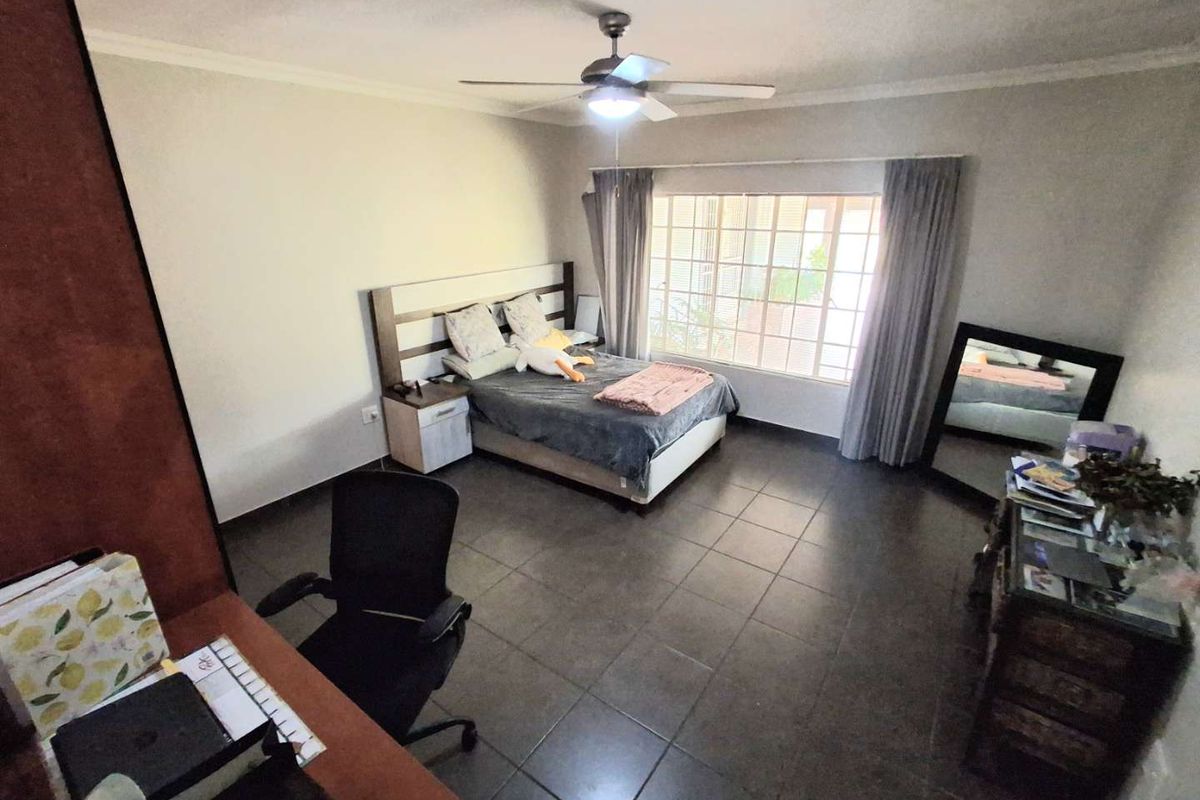 A spacious bedroom featuring tiled flooring, a ceiling fan, and a large window that provides natural light.
