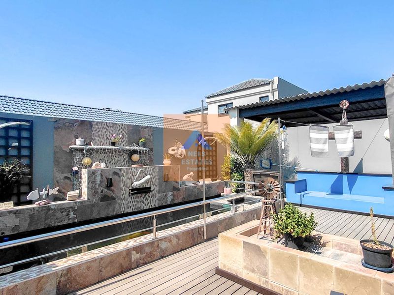 An outdoor patio area featuring a tiled feature wall, wooden decking, built-in seating, and a covered section, ideal for outdoor relaxation and entertainment.