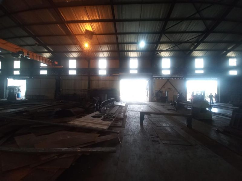 Spacious industrial warehouse featuring a high-clearance steel portal frame, overhead gantry crane, and large roller shutter doors for efficient logistics and operations.