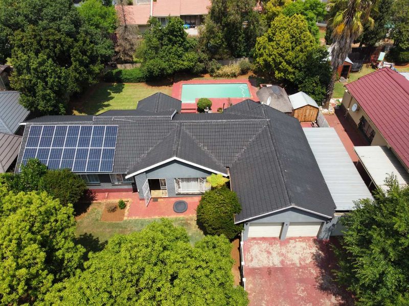 Aerial view of a residential property featuring a tiled roof with solar panels, a swimming pool, a double garage, and a paved driveway.