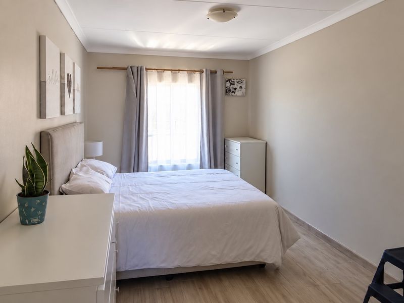 A well-maintained bedroom featuring light-toned laminate flooring, neutral wall finishes, and a window with curtain rod installation.