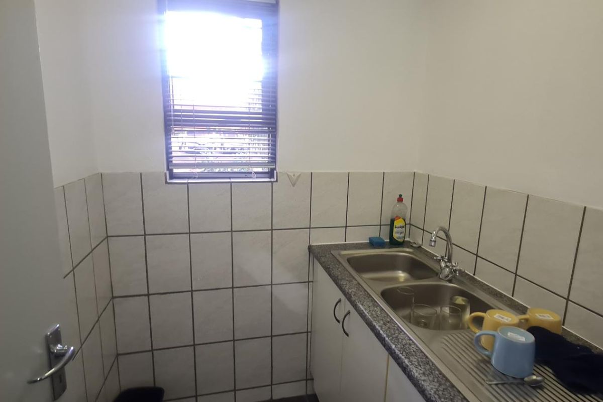 A functional kitchenette area featuring a stainless steel double sink, tiled splashback, and built-in base cabinetry.