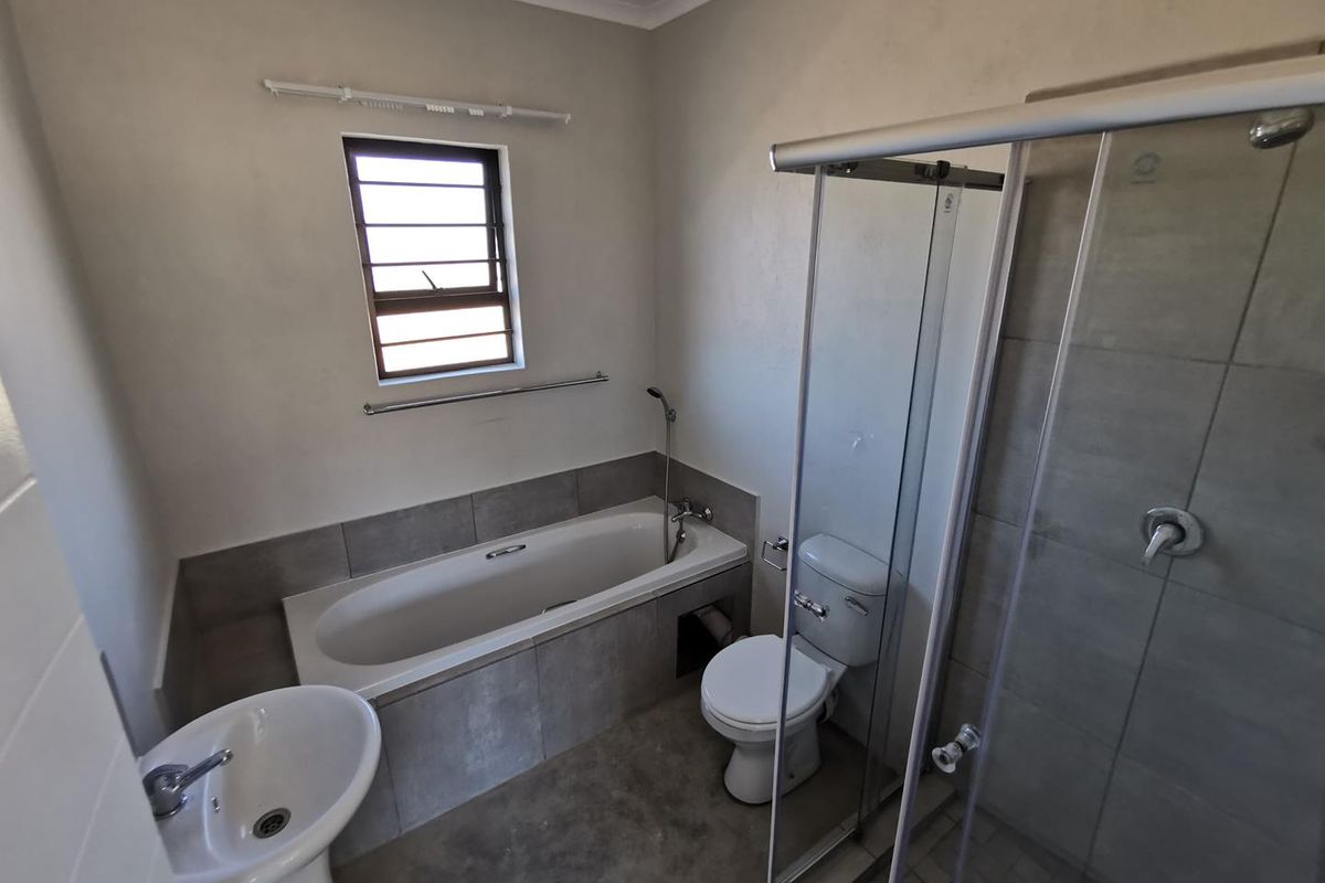 A functional bathroom featuring a built-in bathtub, separate glass-enclosed shower, pedestal basin, and toilet with neutral wall tiling.