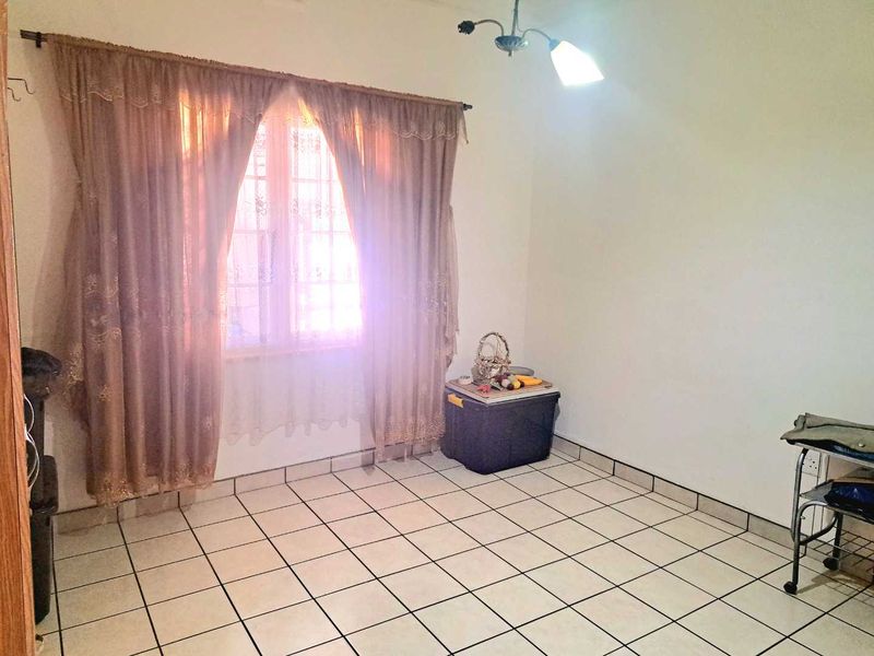 A simple, tiled living area featuring a window with curtains and a central ceiling light fixture, offering a blank canvas for interior design.