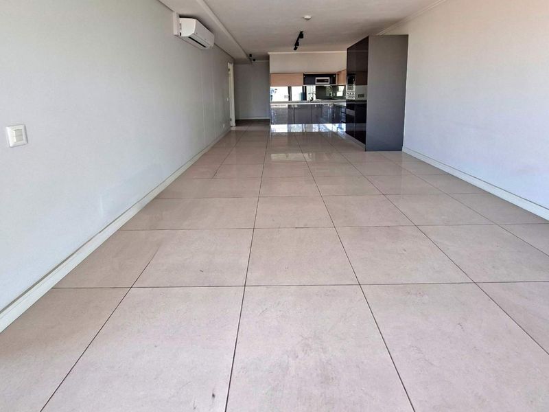 Spacious open-plan living area featuring large format floor tiles, a wall-mounted air conditioning unit, and a modern kitchen with dark cabinetry.