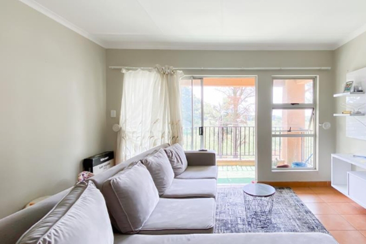 A bright living room featuring tiled flooring, large sliding glass doors leading to a balcony, and built-in shelving units.
