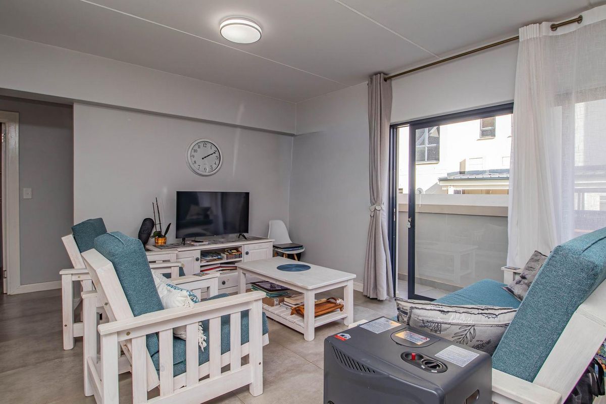 A bright living room featuring tiled flooring, a ceiling-mounted light fixture, and a sliding glass door providing access to an outdoor balcony area.