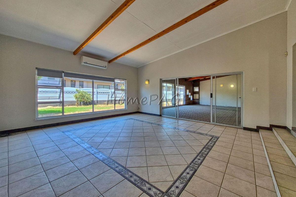 Spacious living area featuring tiled flooring with decorative inlay, exposed timber ceiling beams, split-system air conditioning, and large sliding glass doors leading to a patio.