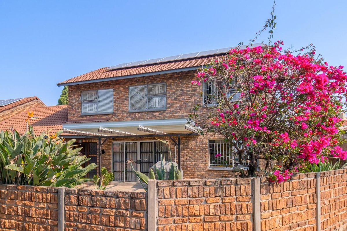 Rear view of a double-story face brick townhouse featuring a tiled roof with solar panels, a covered patio, and a private garden area.