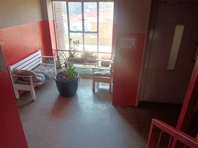 A communal apartment hallway featuring terrazzo flooring, a large metal-framed window, and red painted walls showing signs of wear.