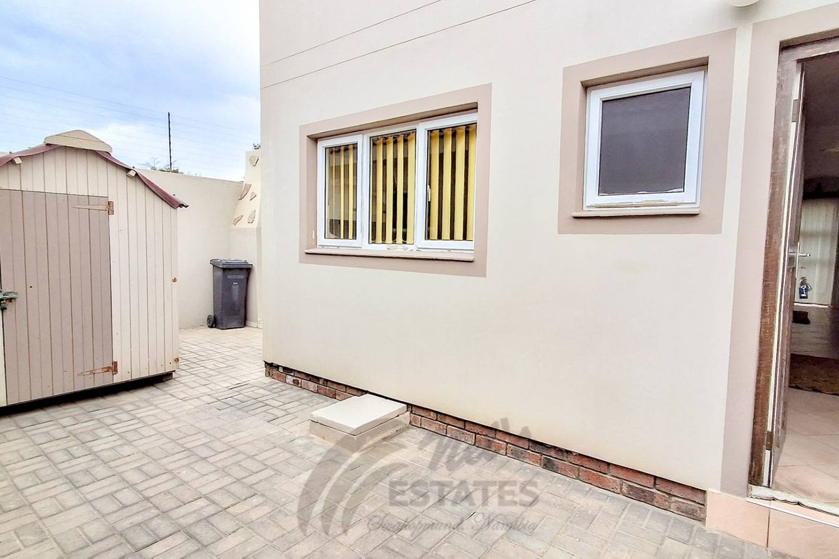 A paved rear courtyard area featuring a storage shed, brick plinth detailing, and access to the interior of the townhouse.