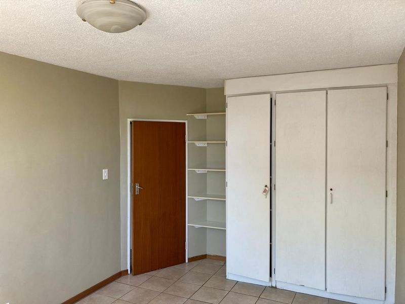 A vacant bedroom featuring tiled flooring, built-in cupboards, and integrated shelving, offering a neutral canvas for personalization.