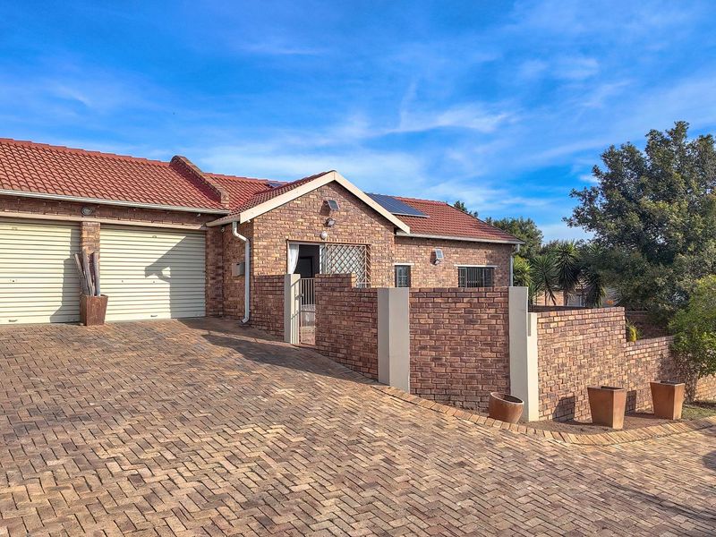 Front view of a cluster home featuring a double garage, brick facade, tiled roof, and a spacious paved driveway.