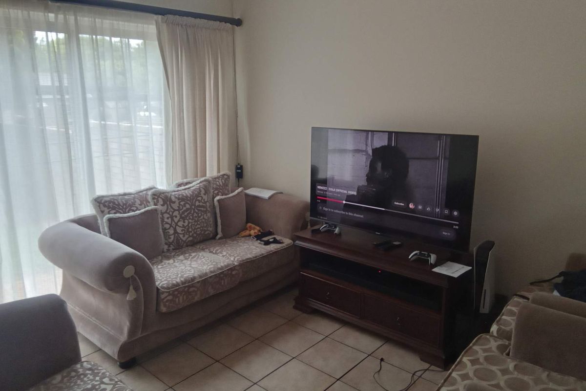 A living room featuring tiled flooring and a large sliding glass door with curtains, providing natural light and access to the exterior.